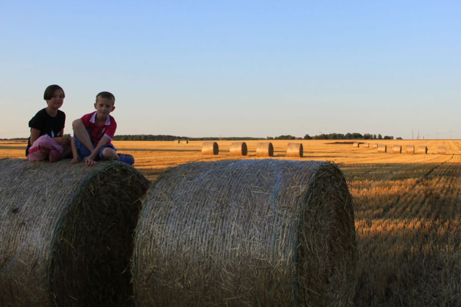 Kinder sitzen im Sommer auf Stroballen auf dem Feld